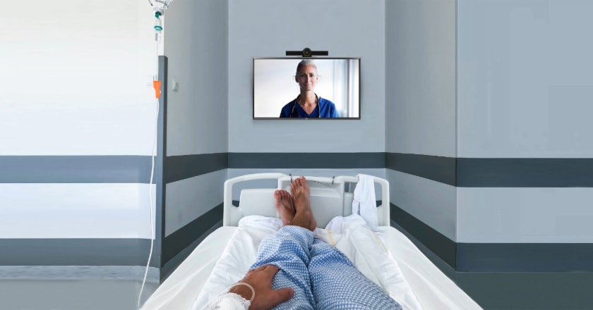 Image is the point of view of a patient laying in bed, looking at a nurse on a television screen