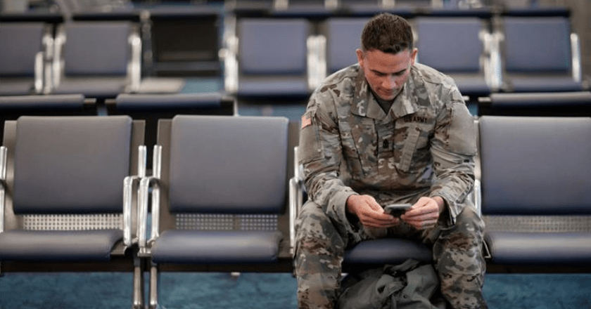 Army service member looking at his phone while waiting for a flight at the airport