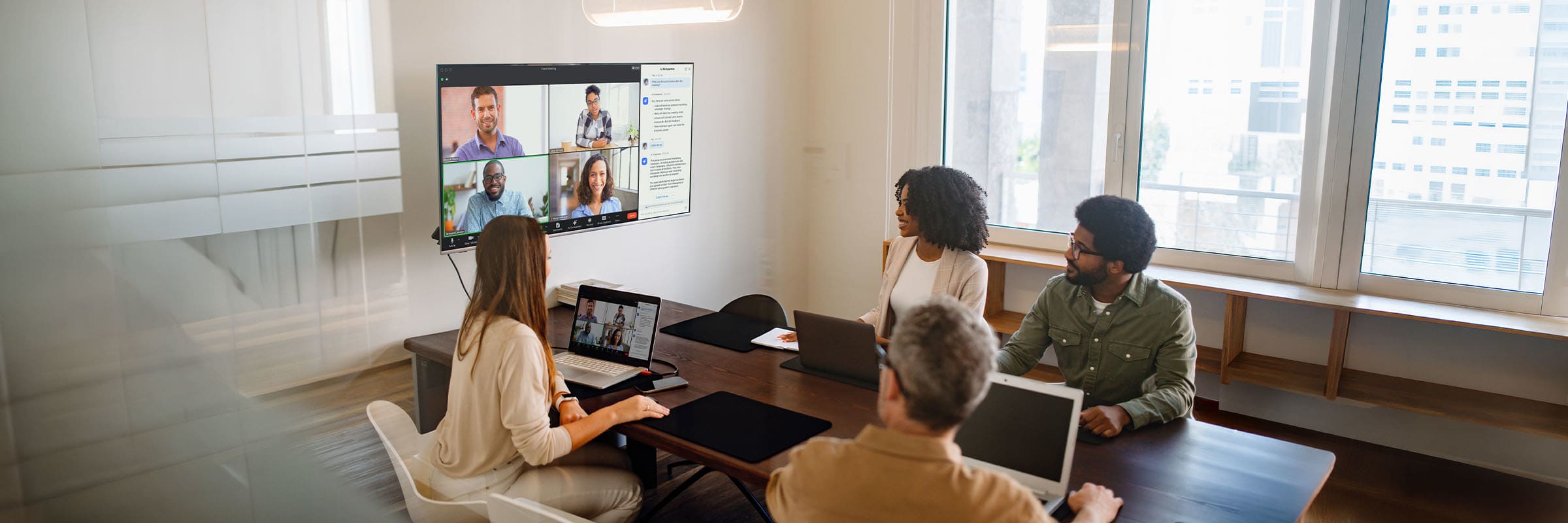 Co-workers in a conference room meeting with colleagues in a Zoom meeting. 