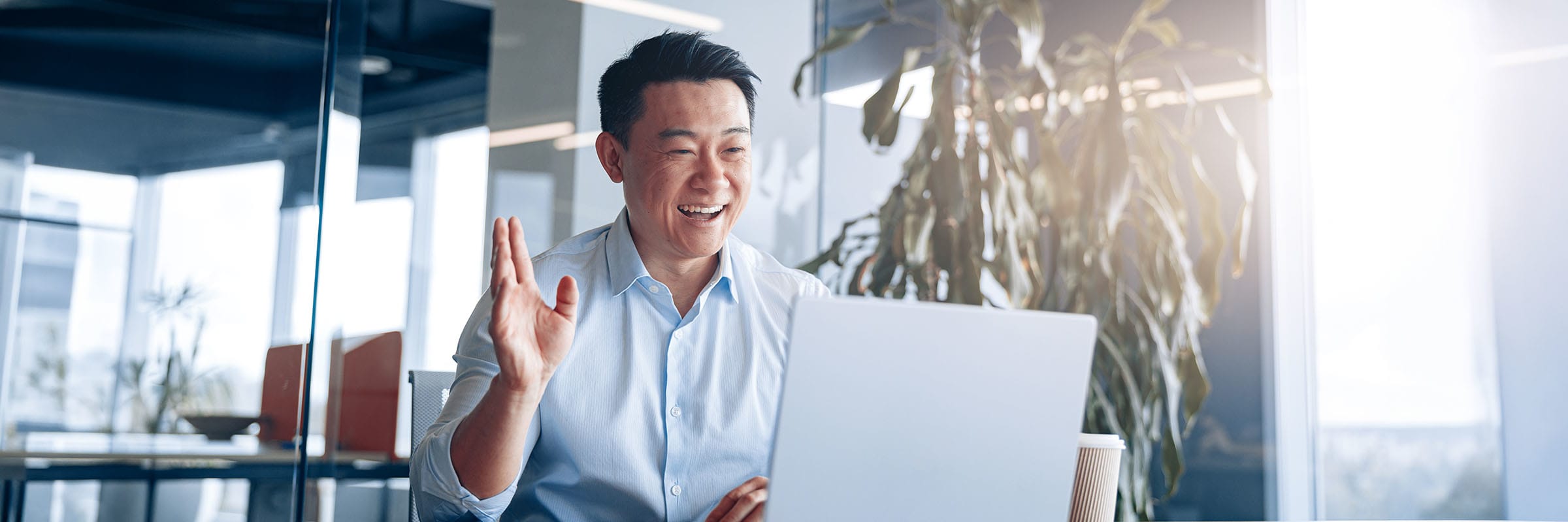 Person in a professional workplace smiling and waving to other participants in a Zoom meeting. 