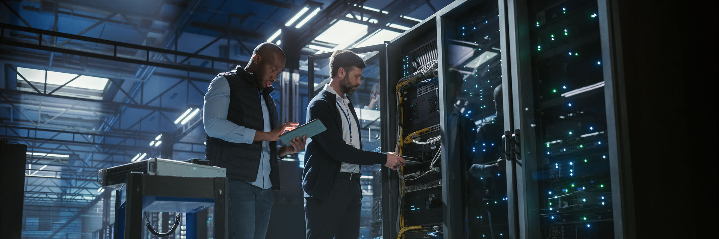 Two men working in a data center. One man is looking at an iPad and the other is adding a component to the rack 