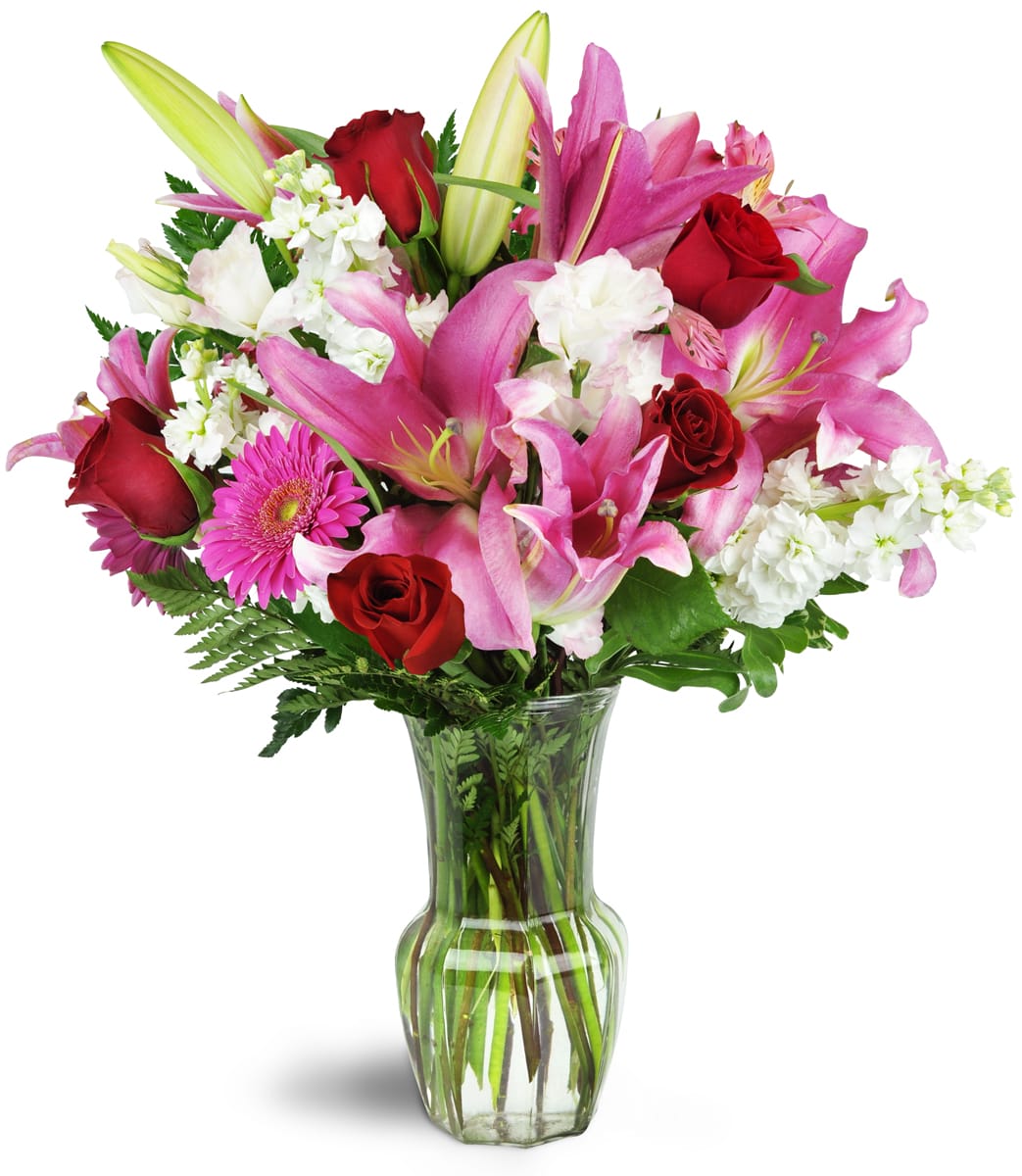 Blushing Heart Bouquet™. An arrangement by AandB Flowers. Deep red roses, lush lilies, and pretty pink Gerbera daisies are arranged in a clear...