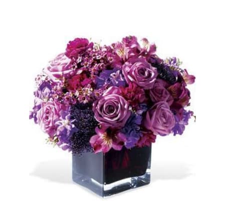 DENSE MIX OF PURPLE ROSES AND OTHER FLOWERS IN A LOW VASE