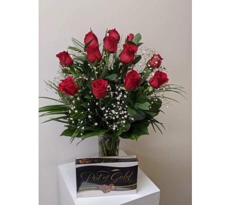 12 Classic Red roses arranged in a vase with a box of chocolates.