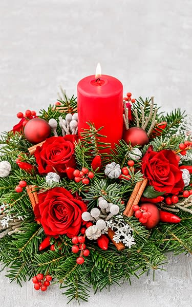 A fresh Christmas floral centerpiece with red roses, berries, pine, and a lit red candle. A fresh Christmas floral centerpiece with red roses, berries, pine, and a lit red candle.