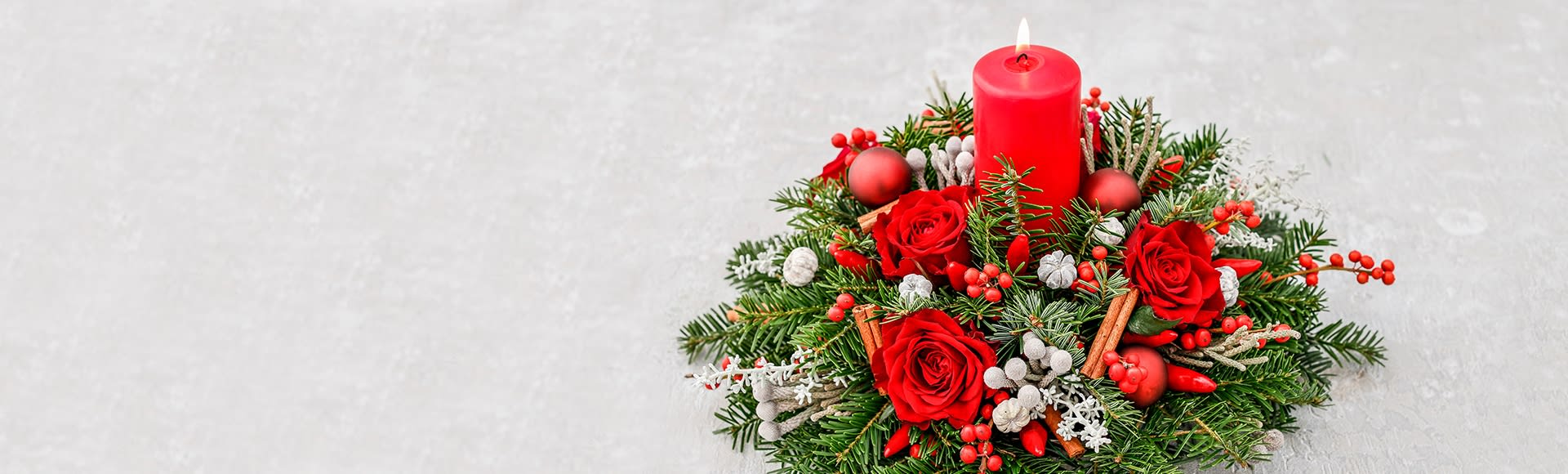 A fresh Christmas floral centerpiece with red roses, berries, pine, and a lit red candle. A fresh Christmas floral centerpiece with red roses, berries, pine, and a lit red candle.