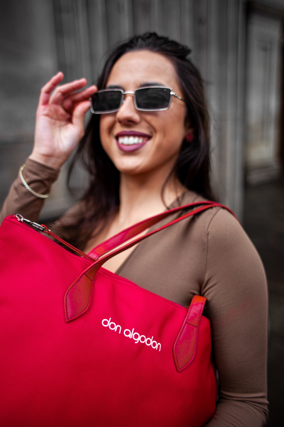 Smiling model in sunglasses carrying a red Don Algodon handbag