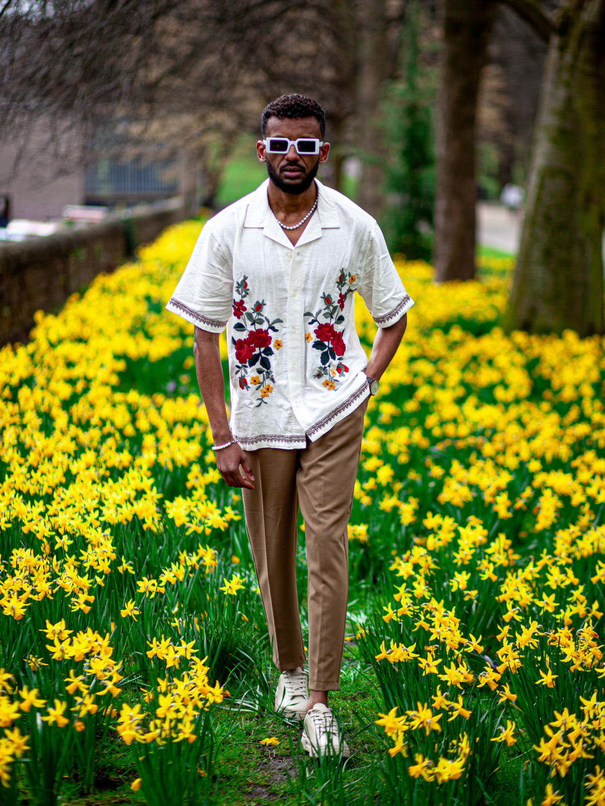 Ehab Ali walking through a field of daffodils in a white floral embroidered shirt