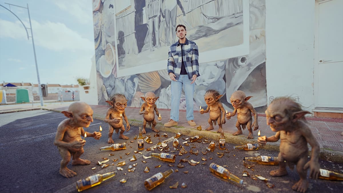 A man surrounded by six CGI goblins holding lit matches, from the Los Duendes music video