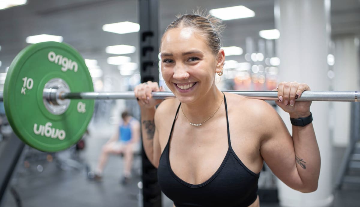 Karina Boniek smiling with a barbell racked across her shoulders in the squat rack