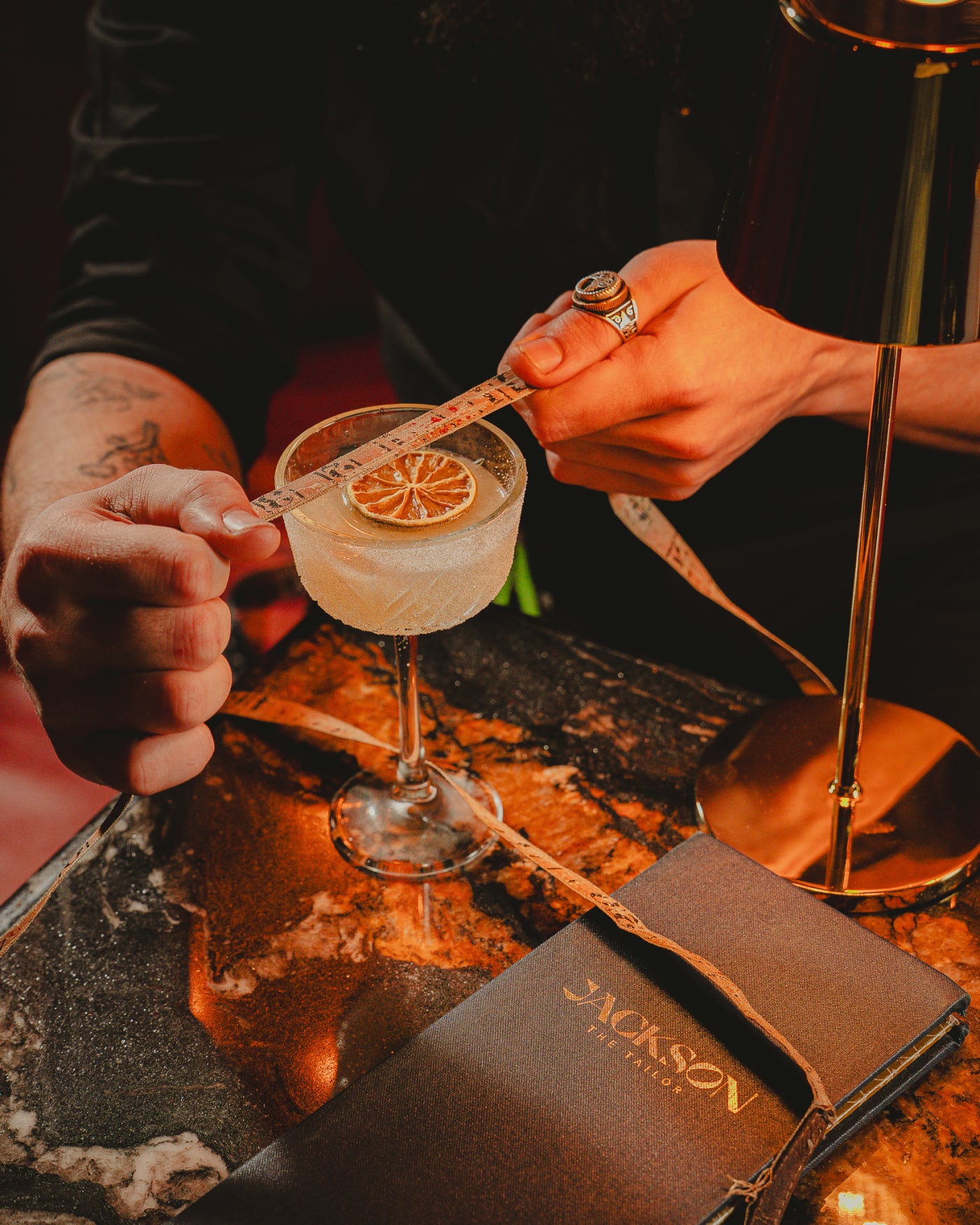 Hands measuring a coupe cocktail with a tailor’s tape at Jackson The Tailor