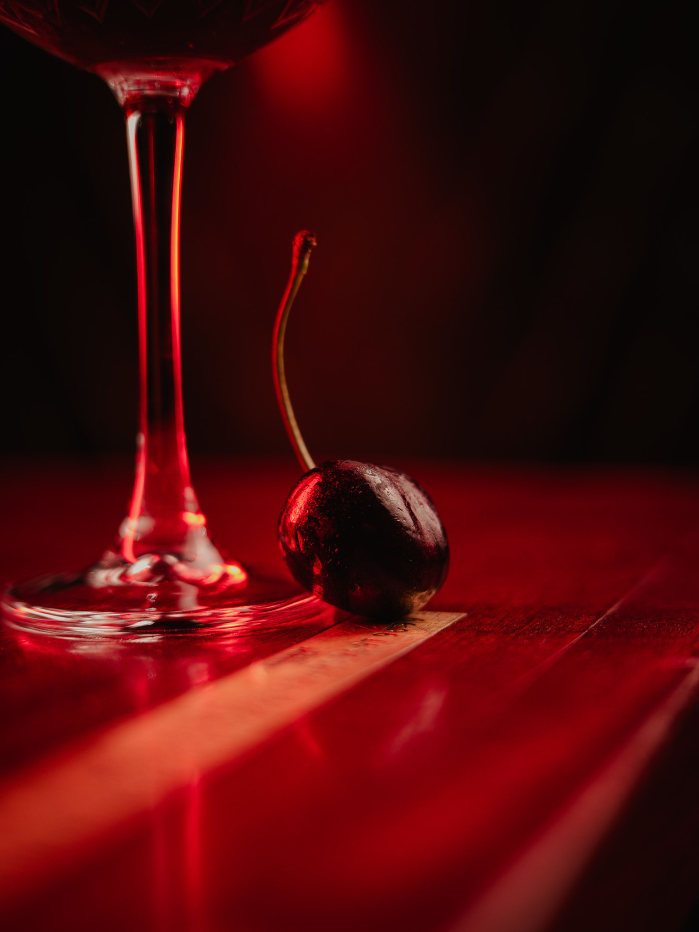Cocktail cherry beside a red coupe, shot low on the red bar at Jackson The Tailor