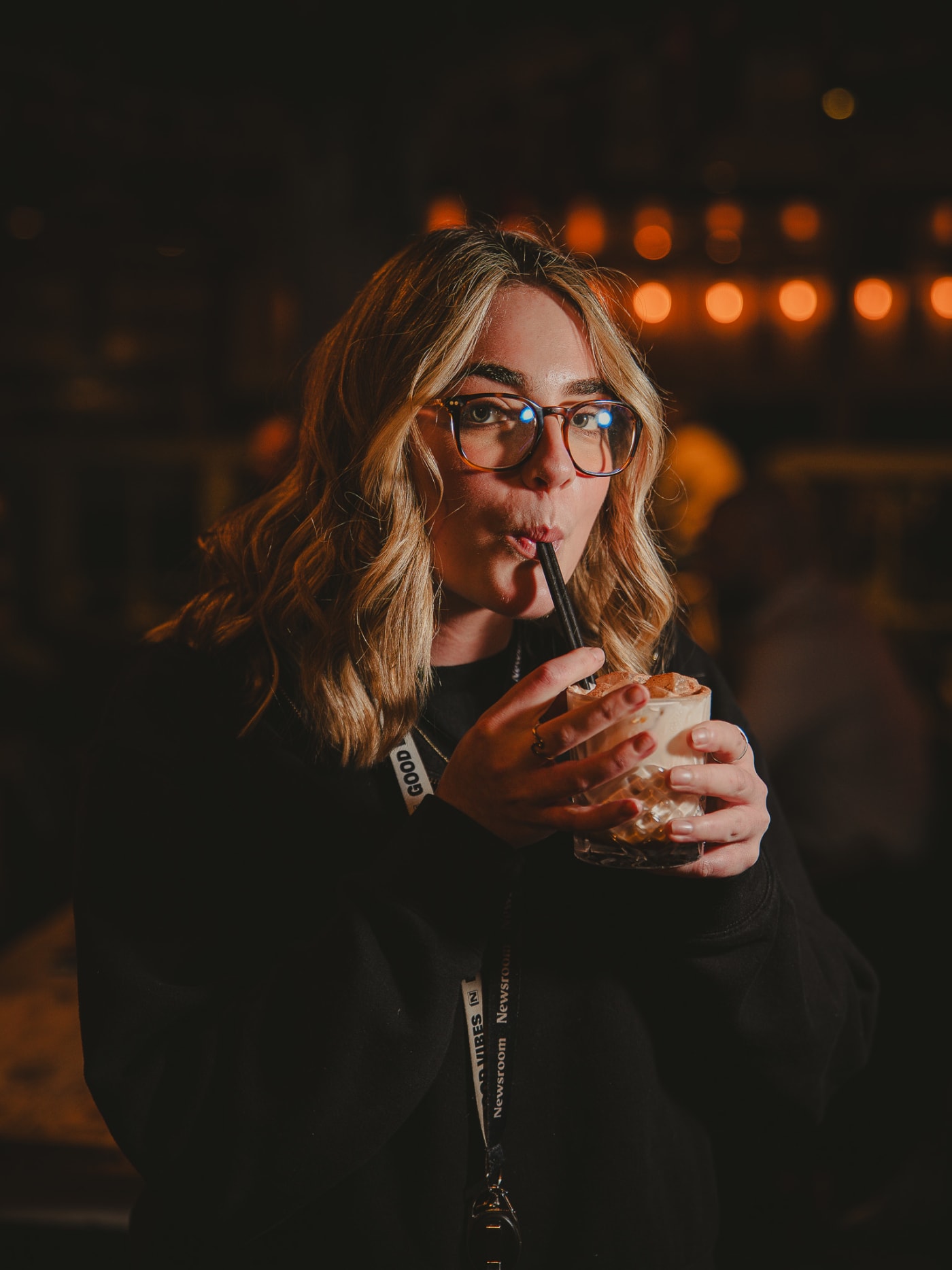 Guest sipping a cocktail through a straw under the warm bar lights at Newsroom, Edinburgh