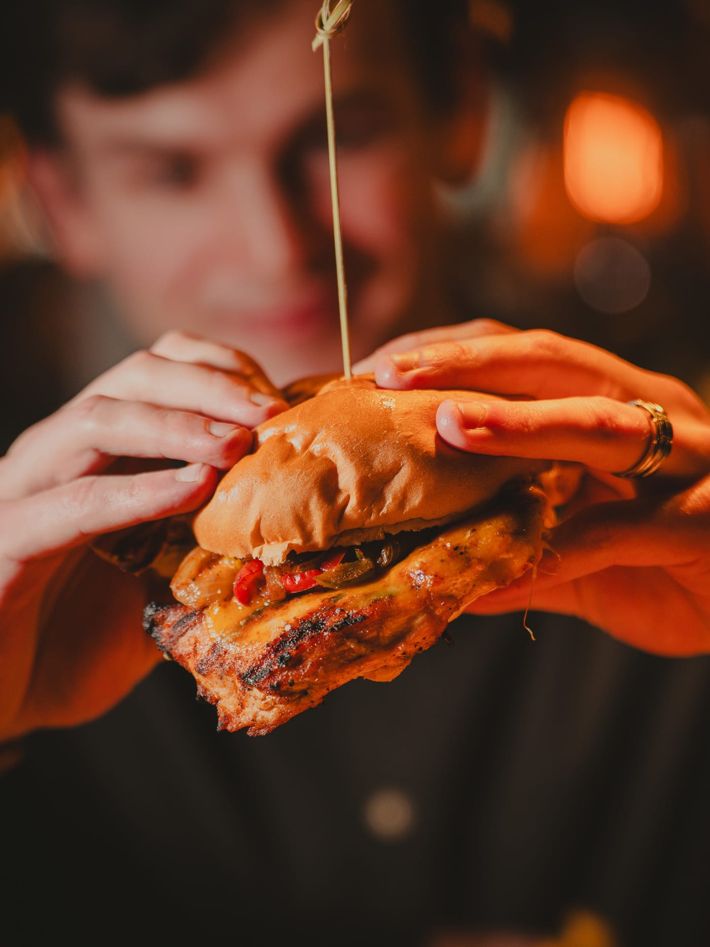 Hands holding a stacked chicken burger with melted cheese and peppers at Newsroom, Edinburgh