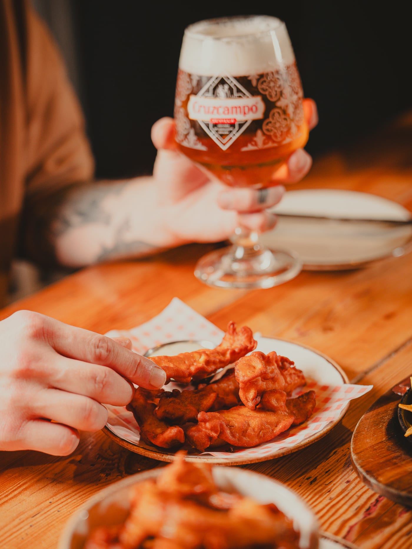 Guest reaching for fried chicken beside a glass of Cruzcampo lager at Newsroom, Edinburgh