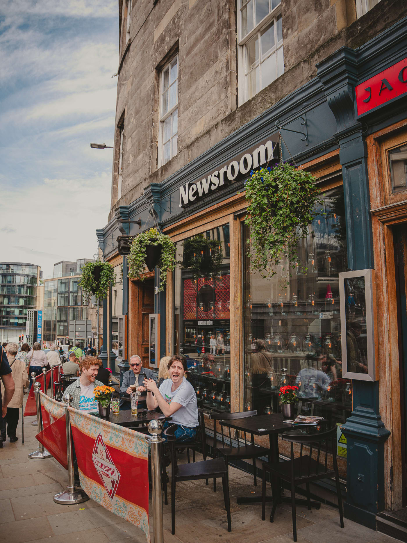 Guests on the outdoor terrace beneath hanging flower baskets outside Newsroom on Leith Street, Edinburgh