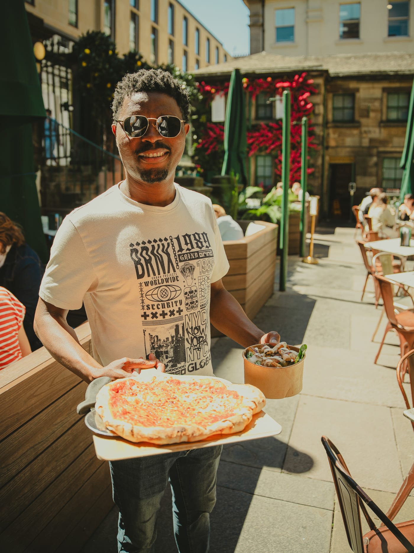 Guest smiling with a fresh pizza on the terrace at Rose Street Garden, Edinburgh