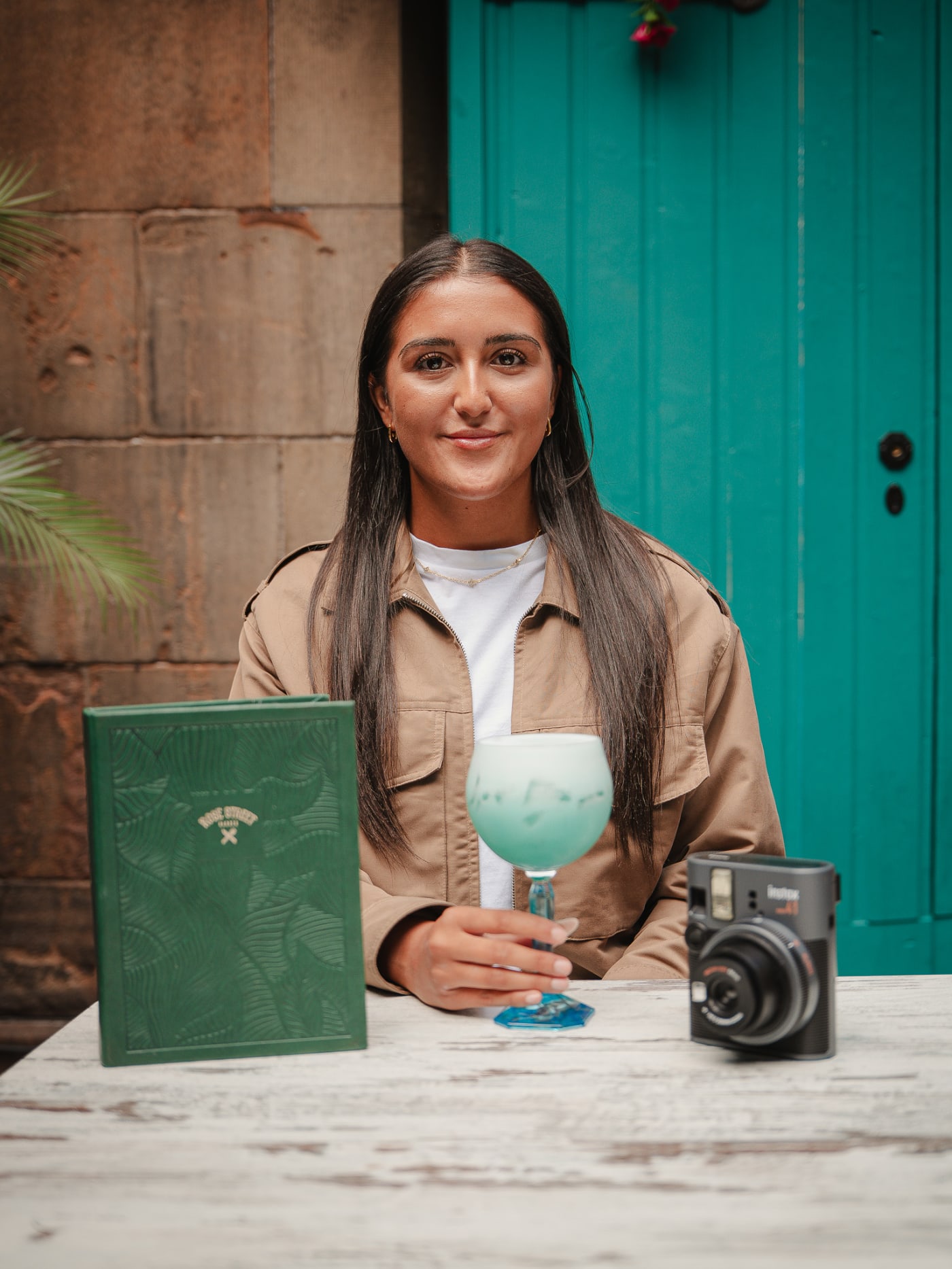 Guest with a blue cocktail and instant camera by the turquoise door at Rose Street Garden, Edinburgh