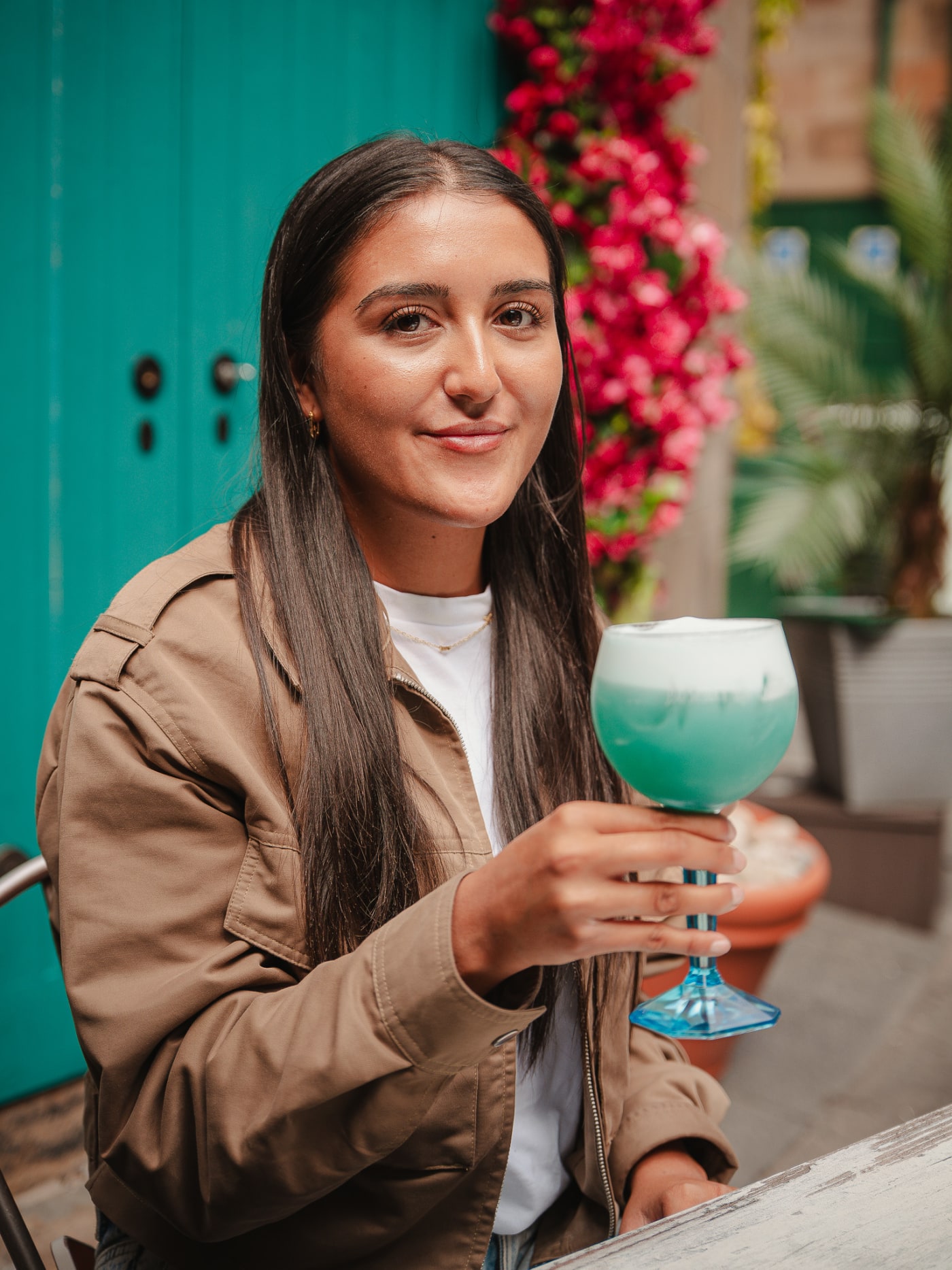 Guest smiling over a blue cocktail by the flower wall at Rose Street Garden, Edinburgh