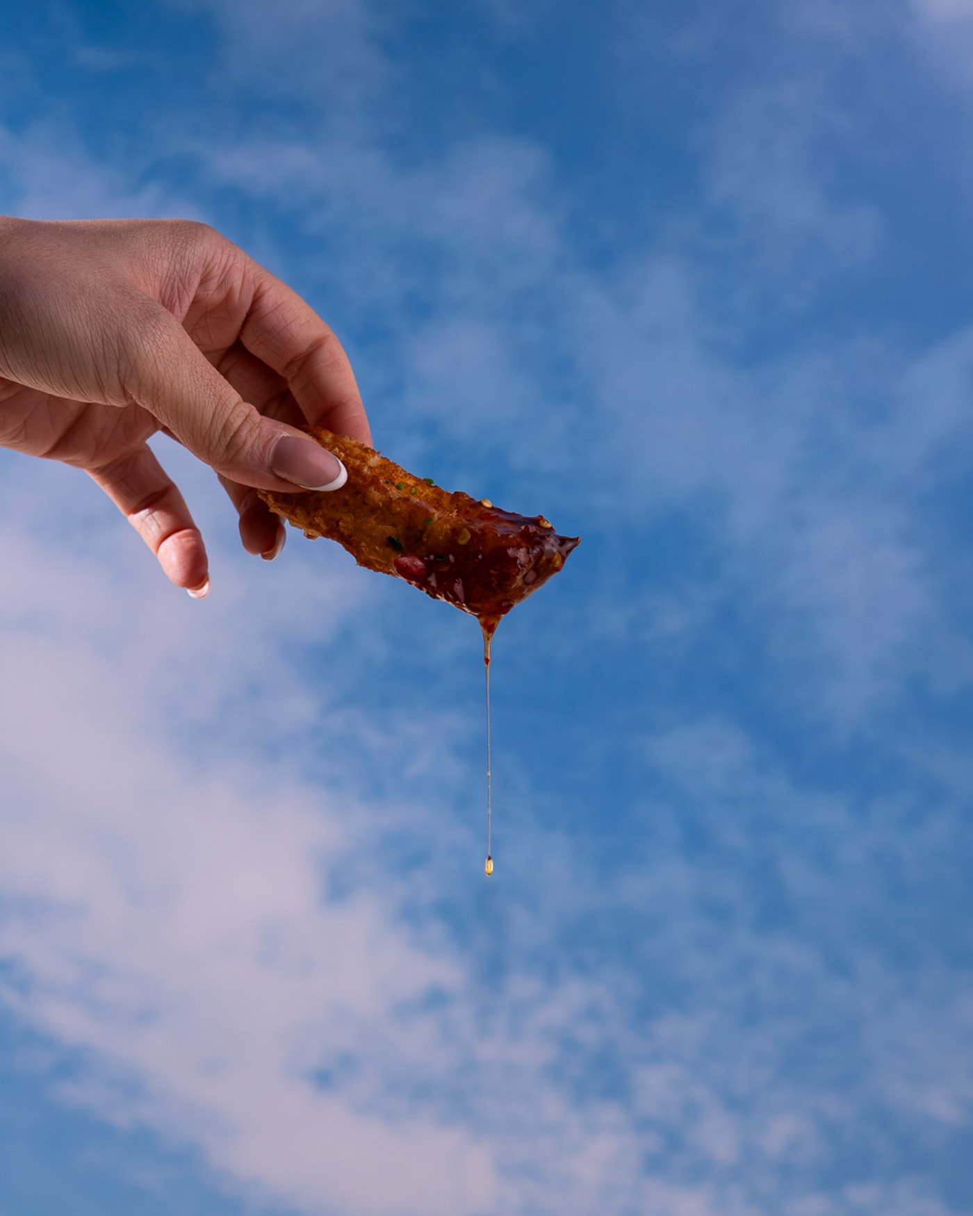 Sticky chicken wing held against the summer sky at Rose Street Garden, Edinburgh