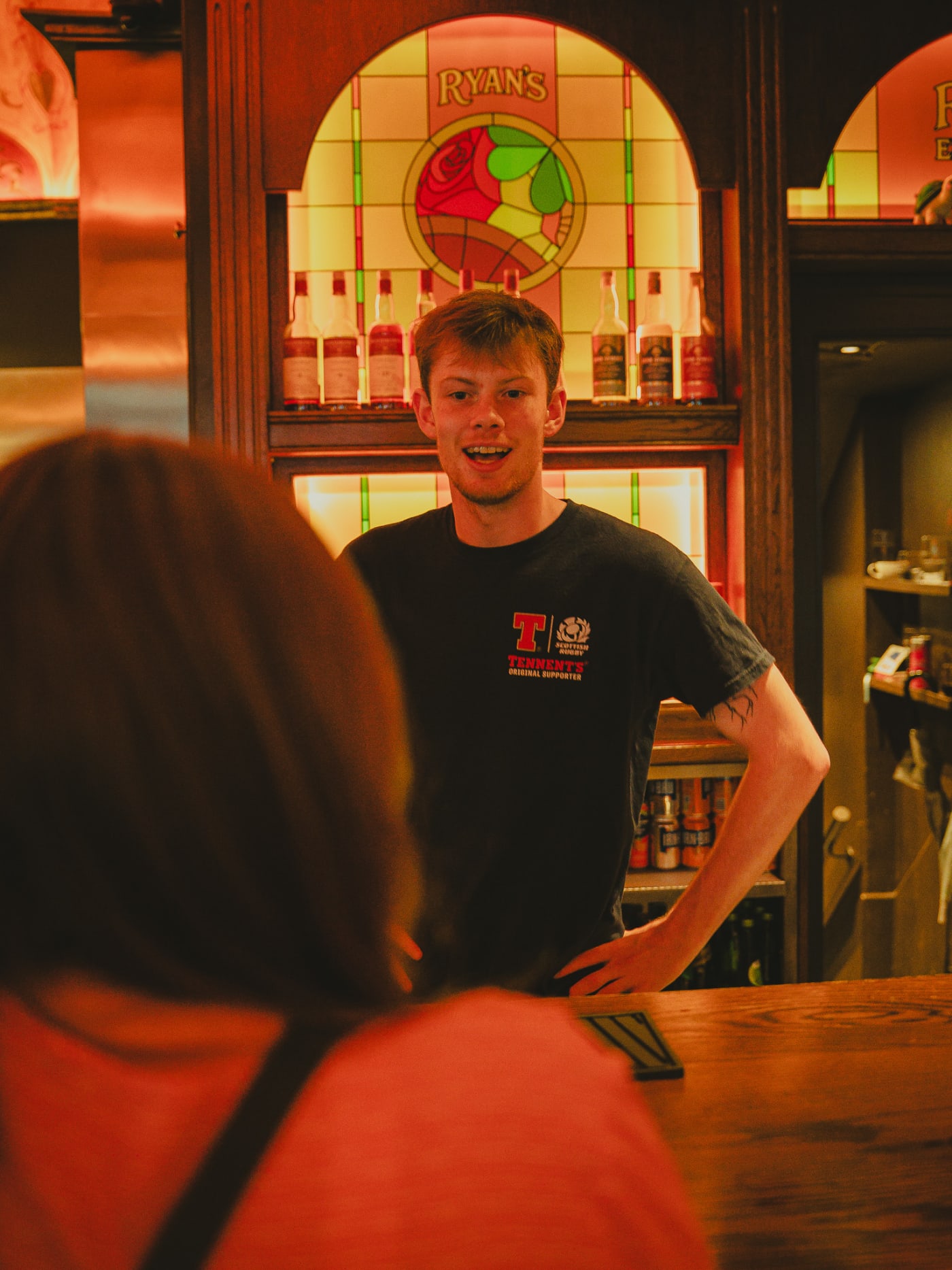Bartender smiling by the stained-glass bar at Ryan's of Edinburgh