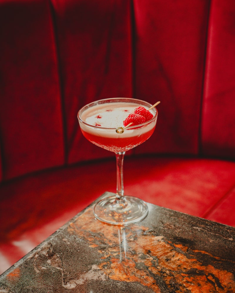 Raspberry coupe cocktail in the red velvet booth at Jackson The Tailor