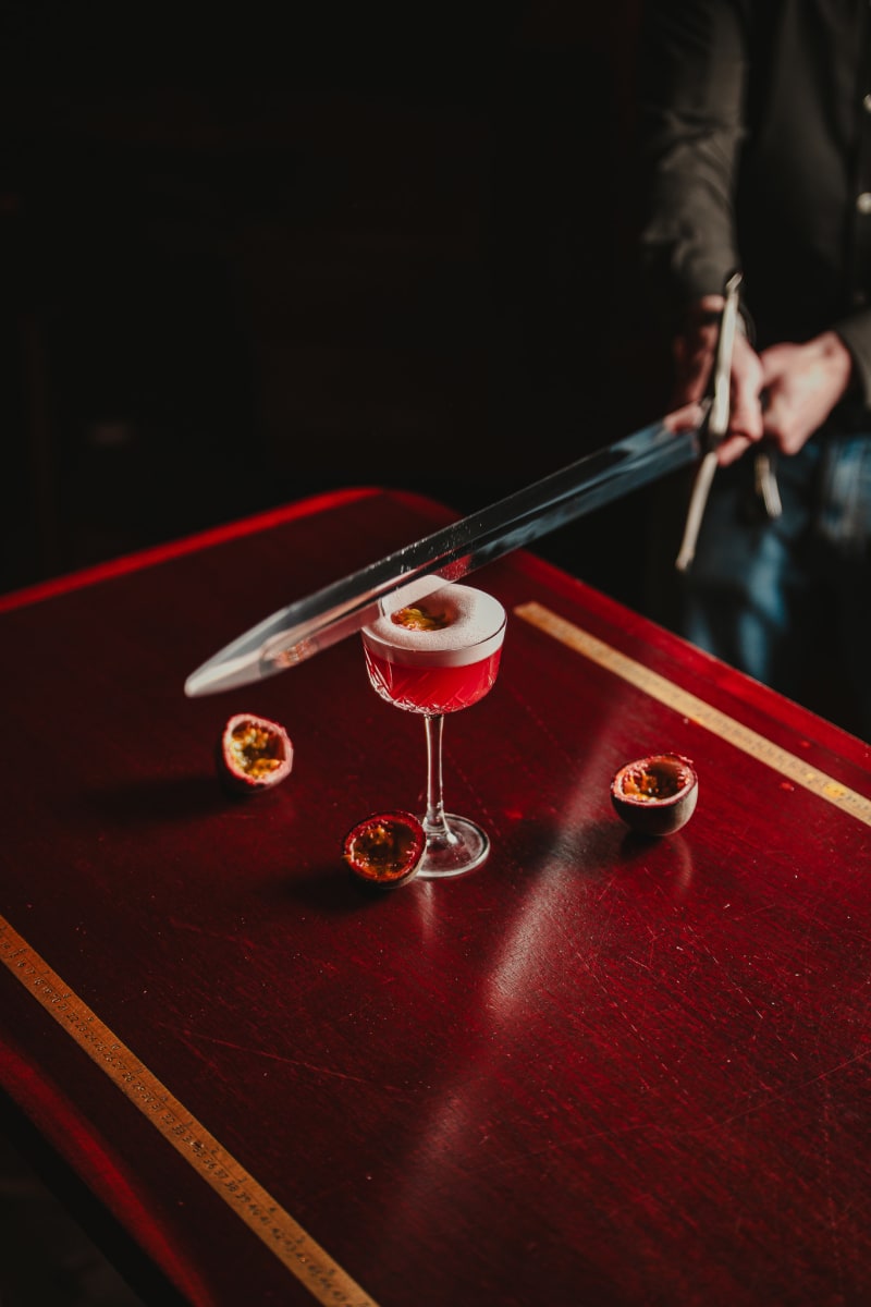 Sword and passion fruit beside a red coupe at Jackson The Tailor