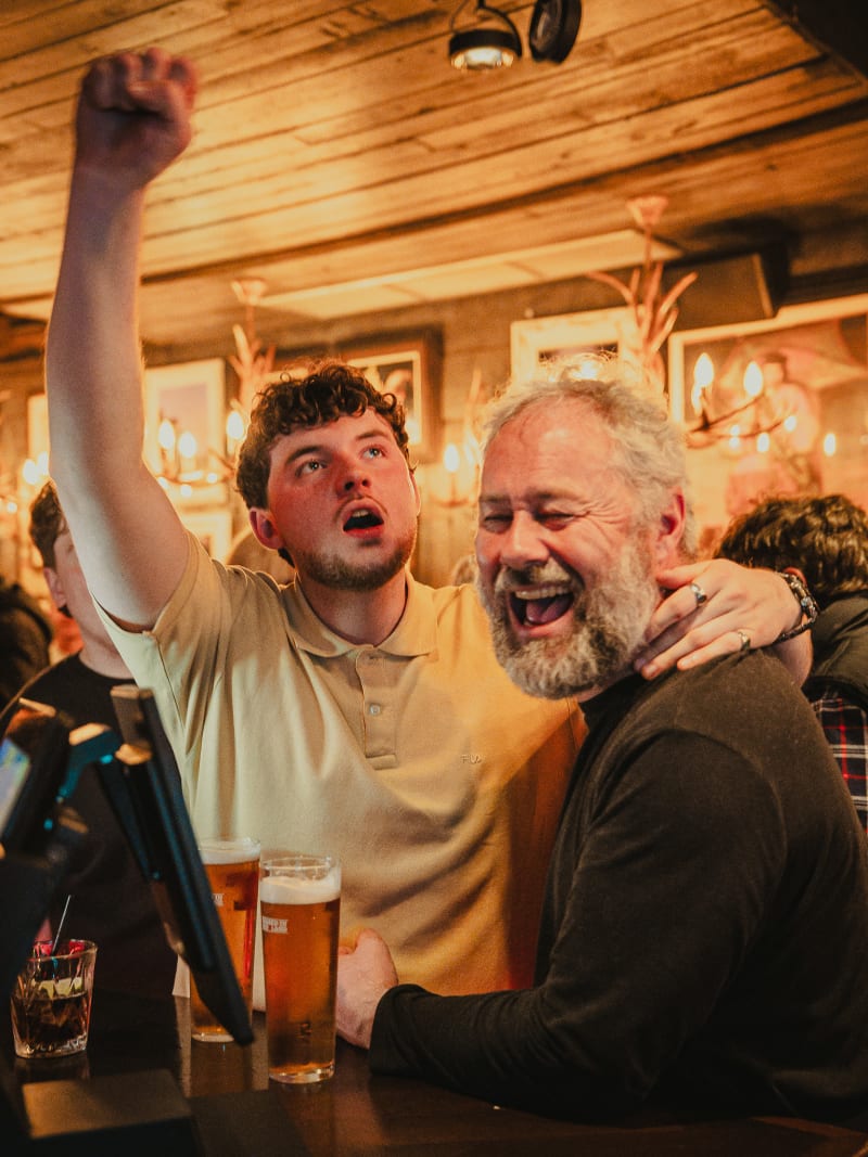 Guests cheering with pints at The Piper's Rest, Edinburgh