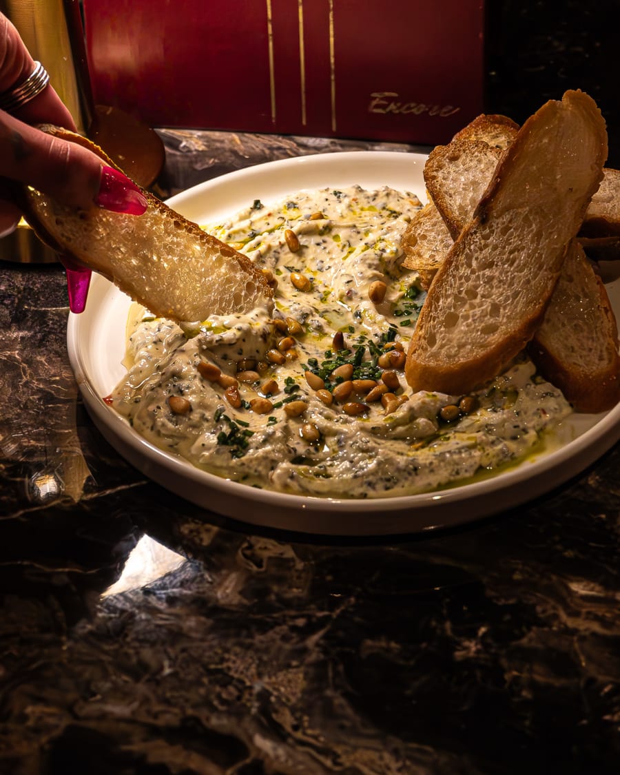 Hand dipping bread into a herb and pine nut dip at Encore