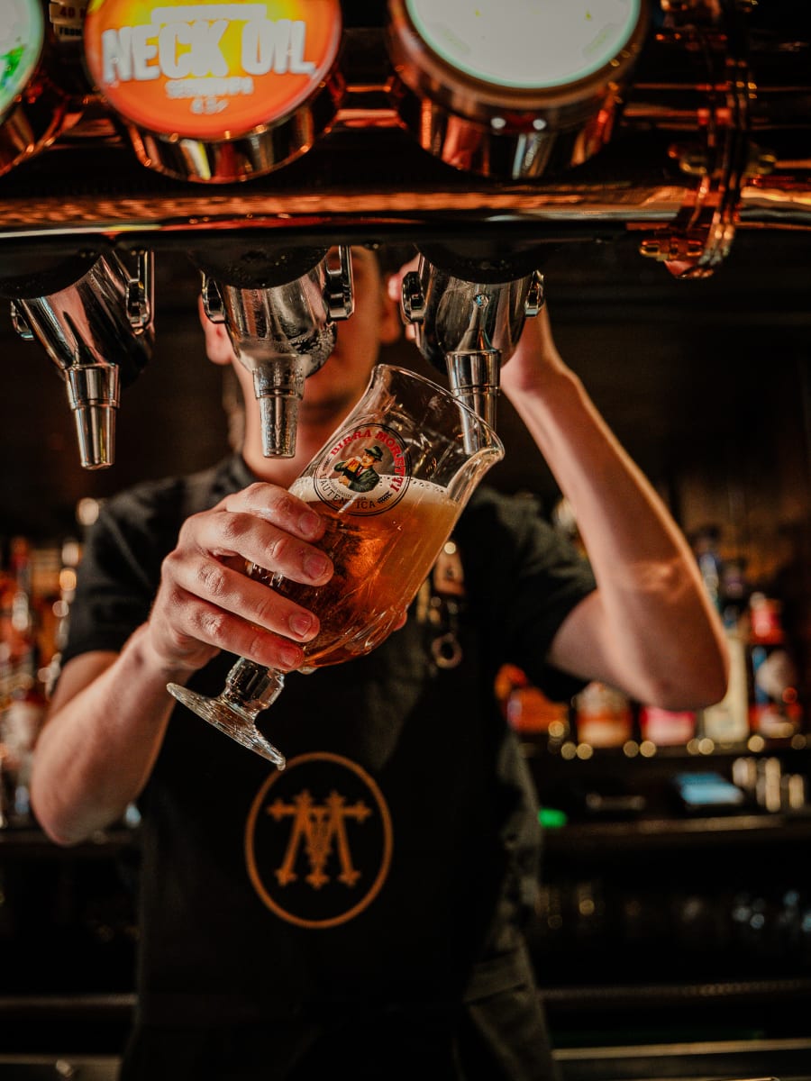Bartender raising a glass while pulling a pint at the copper taps at Merchant Tavern, Edinburgh