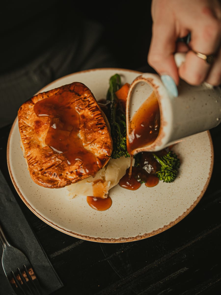 Gravy poured over a golden steak pie with mash and greens at Merchant Tavern, Edinburgh
