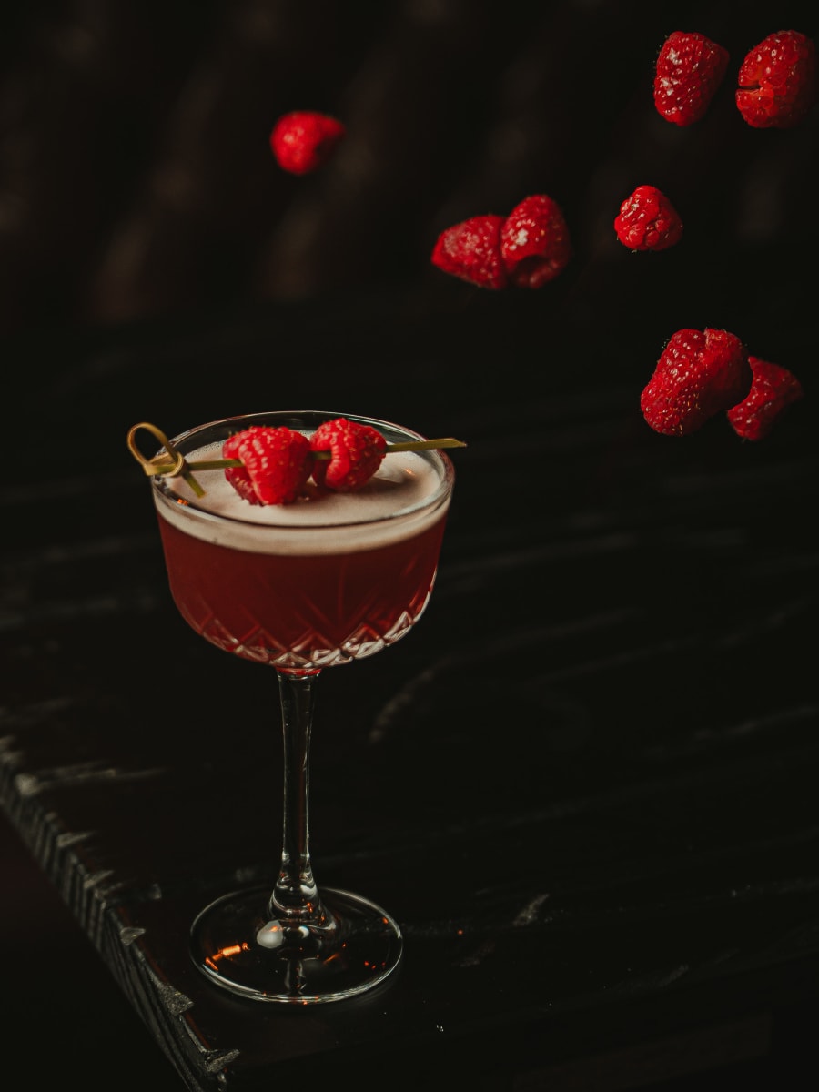 Raspberry cocktail in a crystal coupe with raspberries falling behind it at Merchant Tavern, Edinburgh