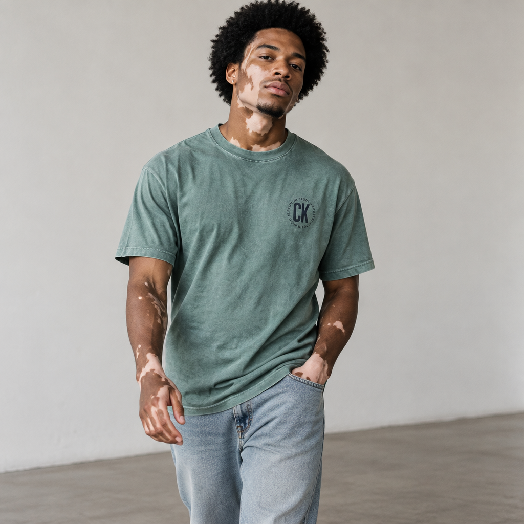 Create a high-fashion photograph featuring a 25-year-old male model with naturally visible vitiligo on his face, neck, and hands, showcasing unique, irregular patterns that realistically follow the body's anatomy. The model has natural black afro hair and appears without visible makeup. His physique is toned, with harmonious proportions and anatomically accurate features. The skin texture should be intricately detailed, revealing pores, subtle imperfections, and natural variances in tone, with a realistic transition between pigmented and depigmented areas from the vitiligo, ensuring an authentic appearance without any artificial or AI-generated effects.

The model is dressed in the outfit from the reference image and adopts a natural walking pose, exuding a confident and elegant demeanor. The photograph is captured with a professional camera and a 50mm lens, utilizing soft natural light, with a shallow depth of field that focuses precisely on the face and skin texture. The background is a clean, minimalist studio setting, visually balanced.

The final image should resemble a professional editorial photograph taken by a real fashion photographer, featuring physically coherent lighting, natural shadows, realistic reflections, correct anatomy, and individually defined hair, while providing an extremely faithful representation of vitiligo. It must avoid a plastic skin appearance, excessive smoothing, CGI-like effects, illustration styles, and any artificial traits associated with image generation.