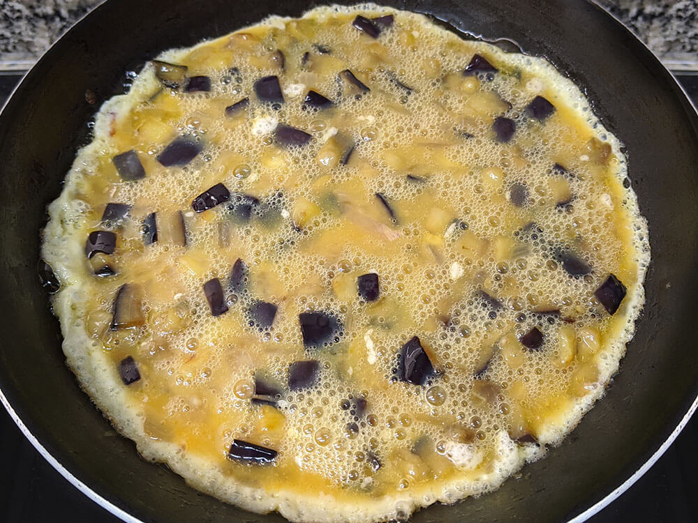 Huevo batido, berenjena y cebolla fritas en sartén.