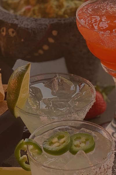 table of chips, guacamole, and three fresh margaritas with strawberries and jalapeno slices