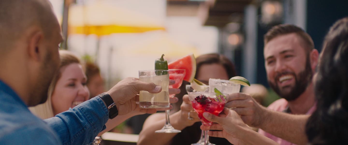 People's hands holding up beverages while dining together on the Uncle Julio's patio