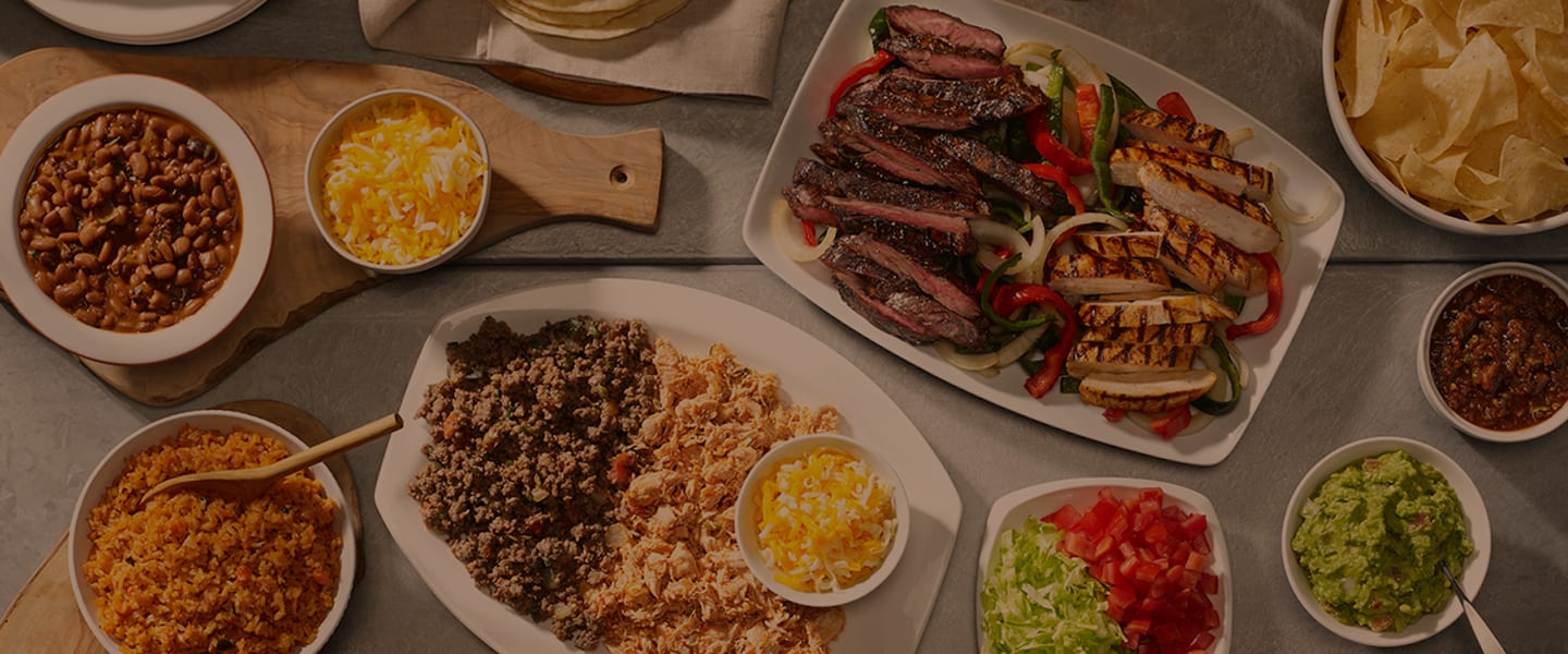 table of chicken and steak fajitas, rice, beans, tomatoes, lettuce, guacamole, and chips