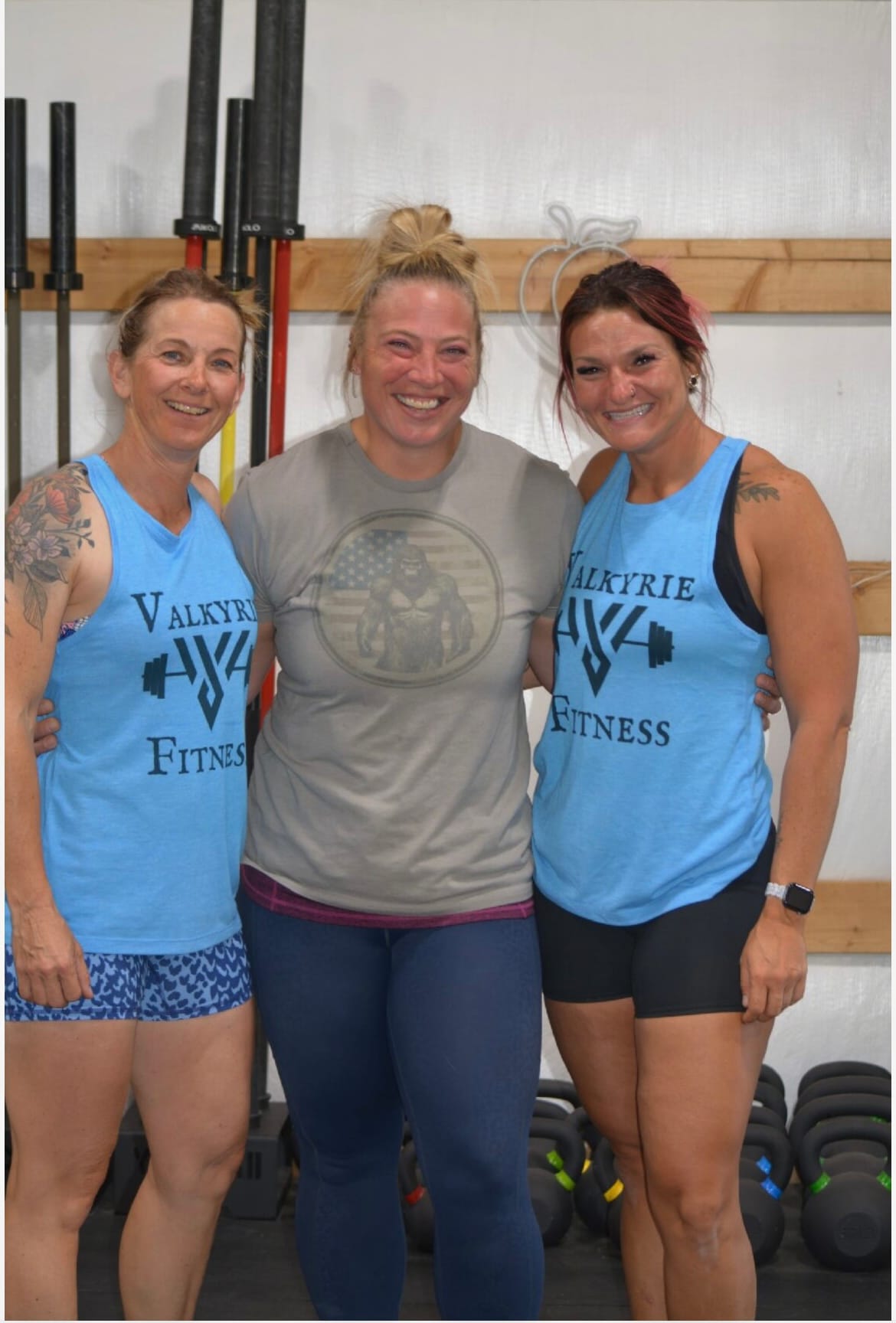 Cali, Lace, and Stephanie standing in front of barbells in the gym.