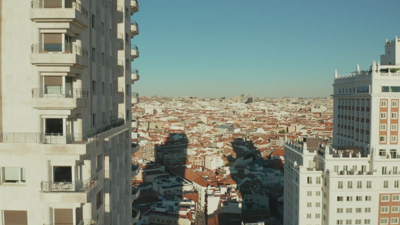 Aerial ascending footage along wall with windows and balconies. Torre de Madrid historic skyscraper and cityscape in background.