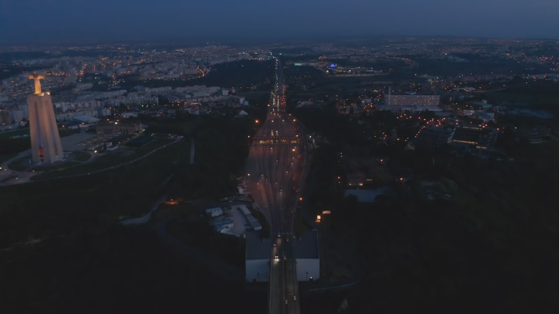 Night aerial view of busy multi lane highway and Santuario de Cristo Rei white monument on the coast of Lisbon, Portugal