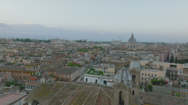 Forwards fly above old residential buildings and historic landmarks in city centre at twilight. Rome, Italy