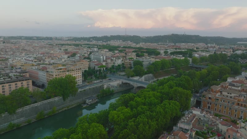 Forwards fly above waterfront. Tiber river lined by green trees passing through city centre. Rome, Italy