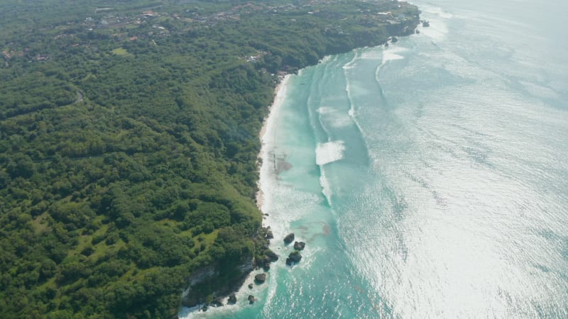 Lush green rainforest vegetation and wild sand beaches on the coastline of Bali. Aerial view of ocean cliffs and turquoise water