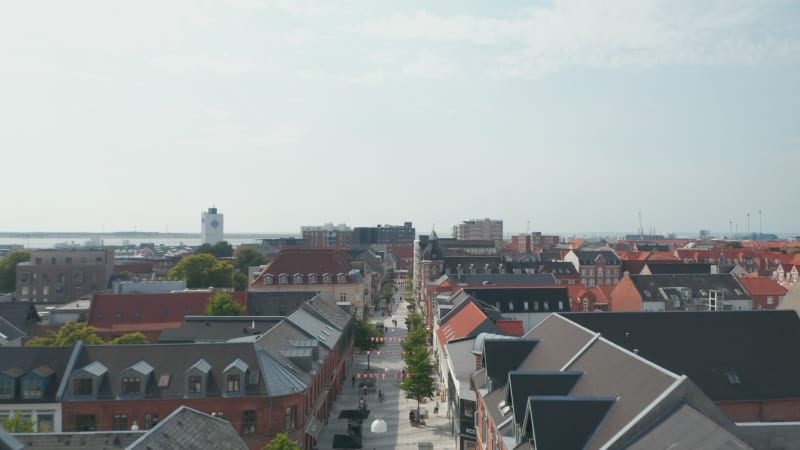 Forward slow flight through Torvegade street in Esbjerg, Denmark, with pedestrians strolling downtown. Aerial dolly revealing Esbjerg harbor in background