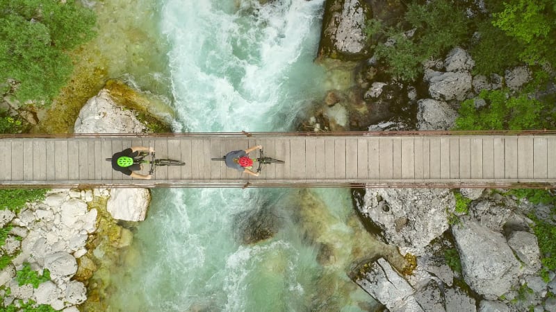 Aerial view of couple crossing a wooden bridge on bicycles.