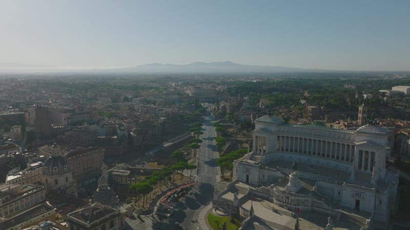 Backwards fly above Piazza Venezia square min historic city centre. Aerial view of famous tourist sights, Vittoriano and Colosseum in distance. Rome, Italy