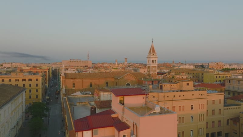 Forwards fly above buildings in city centre, old church with tower lit by morning sunshine. Rome, Italy