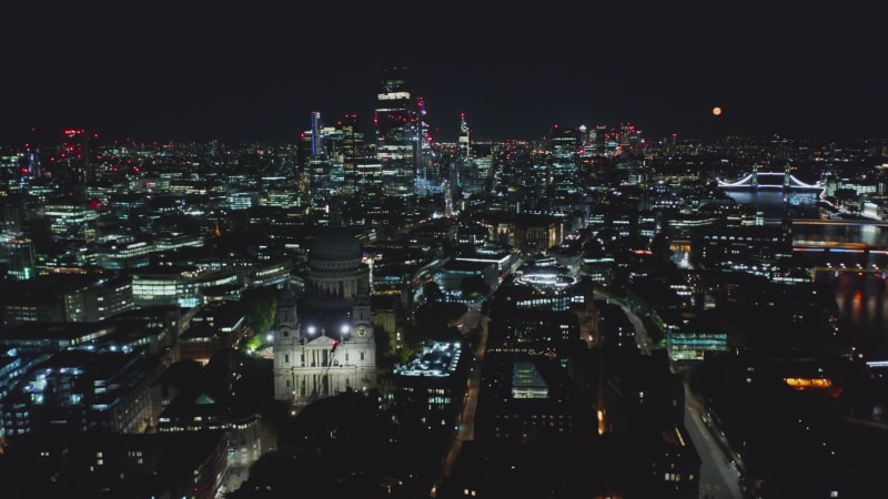 Pull back footage of Saint Pauls Cathedral. Aerial view of night city with tall skyscrapers and Tower Bridge in background. London, UK