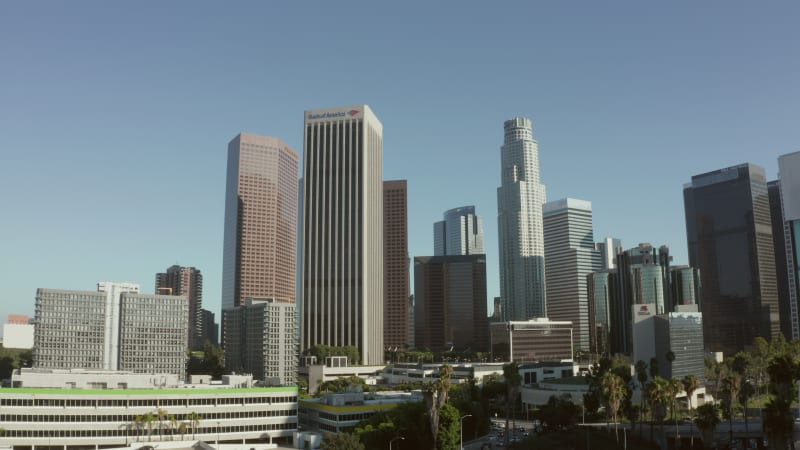 Reveal of Downtown Los Angeles, California Skyline behind building with glass windows at beautiful blue sky and sunny day