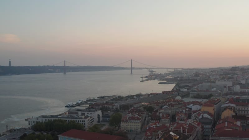 Aerial slider view of Ponte 25 de Abril red bridge across the sea canal in Lisbon, Portugal with houses in old city center